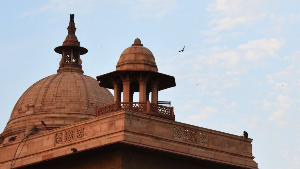 A photo of the top of a red brick building in Delhi with a clear blue sky behind.